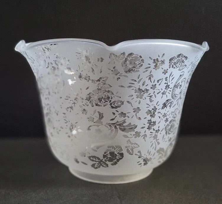 White frosted glass lampshade with a scalloped rim and intricate floral patterns in gray, set against a plain dark background.