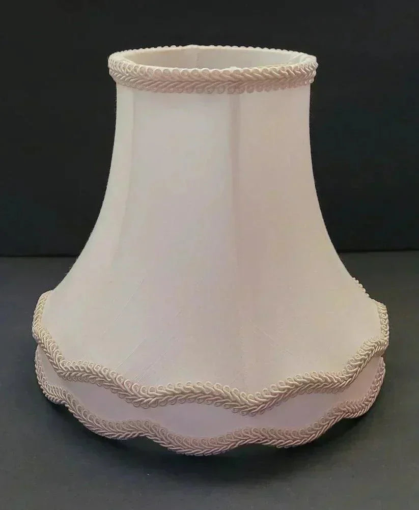A beige fabric lampshade with decorative trim along the top, bottom, and middle edges, set against a plain black background.